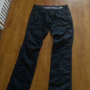 Svarta jeansbyxor G-Star RAW strl 30 - Snygga svarta jeansbyxor från G-Star RAW med coola sömdetaljer och broderad siffra 96 på bakfickan. Byxorna har raka ben, flera fickor och klassisk jeanslook. Perfekta för dig som gillar streetstyle.