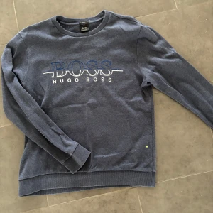 Blå sweatshirt från Hugo Boss - Snygg blå sweatshirt från Hugo Boss med stort broderat logotyptryck på bröstet. Tröjan har rund hals, långa ärmar och ribbade muddar vid ärmslut och nederkant. Perfekt för en chill och stilren look.