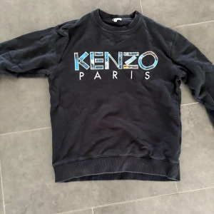 Svart Kenzo Paris sweatshirt - Svart sweatshirt från Kenzo med stort färgglatt Kenzo Paris-tryck på bröstet. Klassisk rund halsringning och långa ärmar. Perfekt för dig som gillar streetstyle och vill sticka ut med en ikonisk logga.