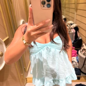 Ljusblå volangig linnetopp - Supersöt ljusblå linnetopp med volangkant och lätt rynk vid bysten. Toppen har en flowy passform och tunna axelband, perfekt för varma dagar. Materialet är tunt och svalt, vilket ger en luftig känsla. Passar dig som gillar en romantisk och somrig stil.