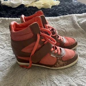 Bruna och korallrosa wedge sneakers - Snygga high-top sneakers med kilklack i brunt och korallrosa. Skorna har snörning, kardborreband och perforerade detaljer. Ovandelen är i mocka och skinn, med vit sula och coola mönsterdetaljer baktill. Dem är lite slitna därav priset.