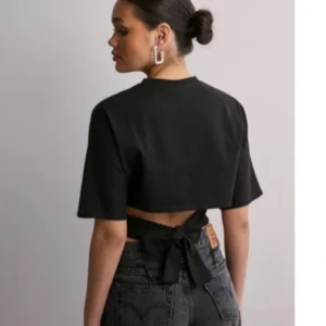 Svart croppad topp med knyt i ryggen - Svart croppad topp med korta ärmar och snygg knytning i ryggen. Perfekt till höga jeans eller kjol för en trendig look. Enkel och stilren design som passar till många tillfällen.