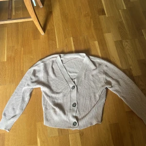 Beige stickad kofta från Lager 157 - Säljer en beige stickad kofta från 157 i storlek M. Koftan har långa ärmar, v-ringning och knäpps med tre stora knappar framtill. Perfekt att slänga på sig när det är lite kyligt ute.