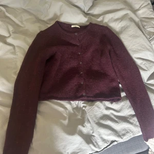 Vinröd croppad kofta med knappar - Mysig vinröd kofta med croppad passform och långa ärmar. Tröjan har rund halsringning och knäppning framtill med små knappar. Perfekt att slänga över en topp för en snygg lager-på-lager-look. Ifrån Gina tricot, använd fåtal gånger. Storlek M men skulle säga att den är liten i storleken så skulle lätta passa en som bär S