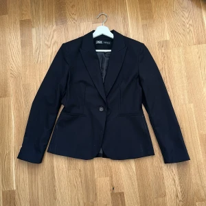 Svart kavaj från Zara - Klassisk svart kavaj från Zara med enkelknäppning. Är använd fåtal gånger och har ingen and tecken på användning. Str. 38 men är liten i storleken så passar 34-36.