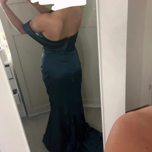 Grön/blå långklänning med slits - Säljer en mörkblå långklänning med offshoulder-modell och öppen rygg. Klänningen har en slits framtill. Perfekt för bal eller fest. Den säljs pågrund av retur ej är möjligt, helt oanvänd. 