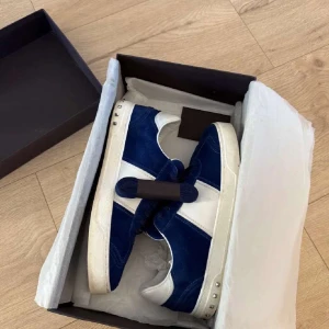 Valentino sneakers i blå mocka och vitt skinn - Säljer ett par snygga Valentino sneakers i blå mocka med vita skinnpaneler och vita sulor. Skorna har rund tå, snörning och diskreta nitar på hälen. Perfekta för dig som vill ha en stilren och exklusiv look.