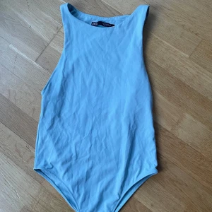 Ljusblå ärmlös bodysuit från Zara - Säljer en ljusblå ärmlös bodysuit från Zara. Perfekt att styla med jeans eller kjol för en enkel och fräsch look. Mjuk bomullskänsla och rund halsringning.