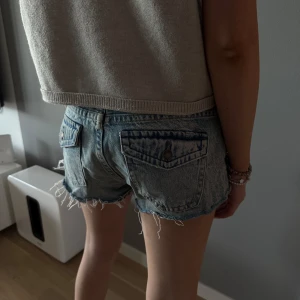 Blå jeansshorts med snygga fickor - Snygga blå jeansshorts med råa franskantsdetaljer och klassiska bakfickor. Shortsen har låg midja och en avslappnad passform, perfekta för varma dagar.