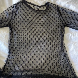 Svart mesh topp med prickigt mönster - Säljer en transparent svart mesh topp med prickigt mönster. Toppen har rund halsringning. Perfekt att styla lager på lager för en trendig look.