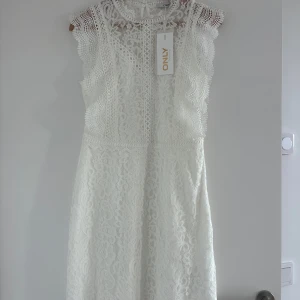 Vit spetsklänning från ONLY - Superfin vit klänning från ONLY i spets med vackra detaljer och rund halsringning. Klänningen är ärmlös och har knappar i nacken. Perfekt för sommarens tillfällen eller student. Aldrig använd.