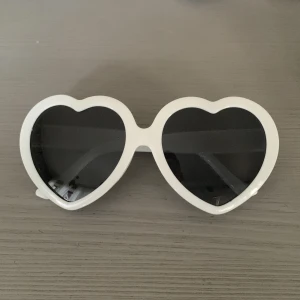 Vita hjärtformade effekt glasögon - Säljer vita effekt glasögon som förvandlar ljus till hjärtan . Glasögonen har hjärtformade bågar och svarta glas. Perfekt accessoar för att sticka ut och ge en lekfull touch till din stil. Passar dig som gillar unika former och vill ha något extra till sommaren.