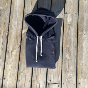 Mörkblå hoodie från Polo Ralph Lauren - Säljer en mörkblå hoodie från Polo Ralph Lauren med klassisk huva och vita snören. Tröjan har en liten röd broderad logga på bröstet och är tillverkad i mjukt bomullsmaterial. Perfekt för en avslappnad och stilren look. Ny pris 2000kr ungefär!
