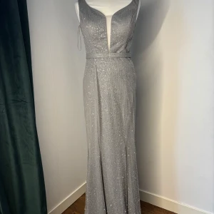 Glittrig silver långklänning med djup v-ringning - Orginal priset: 2500kr säljer för 1199kr. Helt oanvänd och från ett företag som heter party dress,  Eskilstuna 