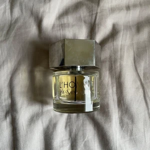 Yves Saint Laurent Parfym - L'Homme från Yves Saint Laurent är en klassisk herrparfym i en rund glasflaska med silverfärgat, sexkantigt lock. Doften är fräsch och maskulin, perfekt för dig som gillar eleganta och moderna parfymer.