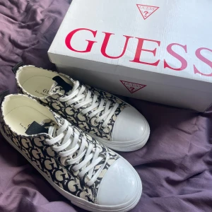 Svarta och vita sneakers från Guess - Säljer ett par snygga sneakers från Guess i svart och vitt med tydligt logomönster över hela skon. Skorna har vita snören, rund tå och platt sula. Använd 1 gång, säljer pågrund av att de var för stora! Skulle säga att de nästan är helt nya. Pris går att diskutera!❤️❤️