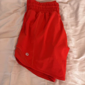 Röda träningsshorts från Lululemon - Snygga röda träningsshorts från Lululemon med elastisk midja och innerbyxa. Perfekta för löpning eller gym. Liten logga på benet och luftig passform för extra komfort.