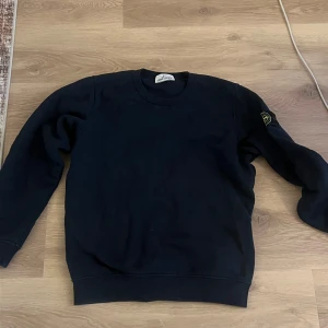 Svart sweatshirt från Stone Island - Säljer en svart sweatshirt från Stone Island med klassisk logotyp-patch på vänster ärm. Tröjan har rund halsringning och långa ärmar. Perfekt för en stilren och avslappnad look