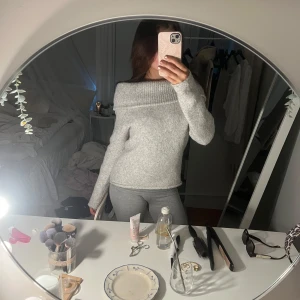 Ljusgrå stickad offshoulder-tröja från Gina Tricot - Supermysig ljusgrå stickad tröja från Gina Tricot med bred offshoulder-krage. Tröjan har lång ärm och är perfekt för lager-på-lager. Snygg till både jeans och kjol, och passar dig som gillar en lite lösare passform.