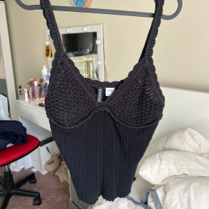 Svart ribbad linnetopp med virkade kupor - Säljer en svart ribbad linnetopp med virkade kupor och smala axelband. Enkel men ändå unik med sin virkade detalj upptill. Storlek M ifrån H&M.