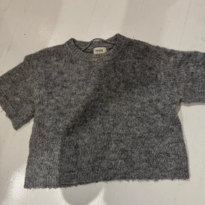 Grå stickad croppad tröja från Aware - Mysig grå stickad tröja från veromoda med korta ärmar och croppad passform. Perfekt till vardags för en avslappnad och trendig look. Rund halsringning och mjukt material som känns skönt mot huden.