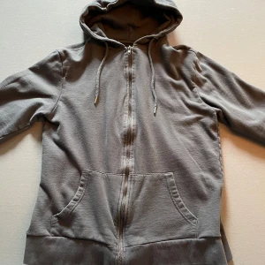 Grå hoodie med dragkedja från 157 - Säljer en enkel och stilren grå hoodie från Lager 157 i storlek M. Tröjan har dragkedja framtill, huva med dragsko och två stora fickor. Perfekt för en avslappnad look.