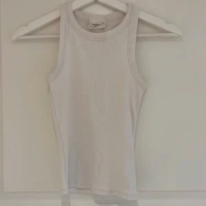 Vit ribbad linnetopp från Gina Tricot - Säljer en klassisk vit ribbad linnetopp från Gina Tricot. Toppen är ärmlös med rund halsringning och har en tight passform. Perfekt att styla till jeans eller kjol för en enkel och fräsch look.