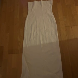 Vit axelbandslös långklänning från LXA - Säljer en stilren vit axelbandslös långklänning från LXA. Klänningen har en ribbad kant upptill och är figurnära med en enkel, elegant design. Perfekt för dig som gillar minimalistisk stil. Storlek L