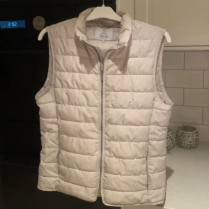 Benvit dunväst från Bläck - Säljer en vit dunväst från Bläck i storlek Small som är extremt stilren och enkel att matcha. Västen är från MQ köpt för 1199kr och färgen är numera helt slutsåld. 