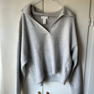Ljusgrå stickad tröja med krage - Mysig ljusgrå stickad tröja från H&M med v-ringning och bred krage. Tröjan har långa ärmar. Använd knappt.