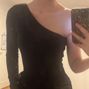 Topp - Säljer en svart oneshoulder topp med lång ärm på ena sidan från NA-KD. Snygg och stilren design som passar perfekt till många olika outfits. Så fint till en utekväll 😻 den har använts ett fåtal gånger men ser fortfarande ut att vara i mycket bra skick 🫶 kontakta för mer information 