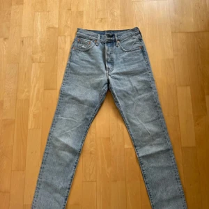 Levis 501 ljusblå jeans - Klassiska Levis 501 jeans i ljusblått med raka ben och femficksmodell. Byxorna har knappgylf och Levis ikoniska läderpatch bak i midjan. Perfekta för en avslappnad och tidlös stil.