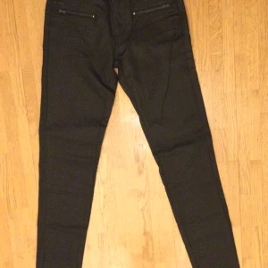 Svarta byxor med dragkedjedetaljer från La Redoute 34 - Snygga svarta byxor från La Redoute med två dragkedjor framtill och klassisk knappstängning. Byxorna har en smal passform och är perfekta för en stilren look. Materialet känns mjukt och stretchigt för extra komfort. 98% bomull,  % elastan Beninnerlängd: 83 cm Midja: 68 cm Oanvända, med tags! Katter finns i hemmet!