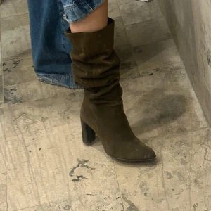 Mörkgröna höga boots i mocka - Säljer ett par snygga mörk gröna boots i mocka med hög skaft och klack. Man kan välja att ha dem slouchy eller högt baserad på hur du vill ha. Perfekta att styla med jeans eller klänning. 