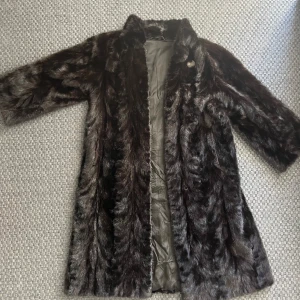 Lång pälsjacka från Bergströms Gefle - Säljer en klassisk lång pälsjacka i mörkbrunt från Bergströms Gefle. Jackan har lång ärm, hög krage och knäppning framtill. Fodrad insida med broderade initialer. Perfekt för kalla dagar när du vill känna dig extra lyxig.