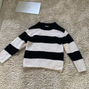 Randig stickad tröja från Gina Tricot - Säljer en mysig stickad tröja från Gina Tricot i storlek 134/140. Tröjan har breda svarta och vita ränder, rund halsringning och långa ärmar. Perfekt för kyligare dagar och enkel att matcha med jeans eller kjol.💕💕