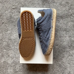 Maison Margiela espadrilles Blå sneakers med flätad sula - Säljer ett par blå sneakers med canvasöverdel och flätad, naturfärgad sula. Skorna har snörning och en platt gummisula med vågigt mönster undertill. Perfekta för en avslappnad stil.retail 7000