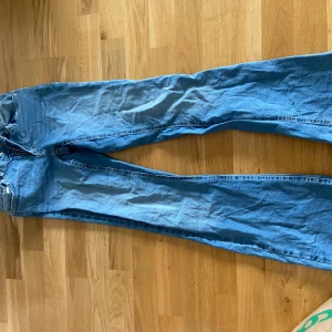 Ljusblå jeans med nitar på bakfickan - Säljer ett par ljusblå jeans med raka ben och snygga nitar på bakfickan. Klassisk femficksmodell med dragkedja och knapp framtill. Perfekta för dig som vill ha en cool detalj på dina jeans!      Sista bild syns det en liten slitning jämte bakfickan, syns knappt när dem är på.🥰