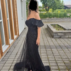 Svart glittrig långklänning med offshoulder - Säljer en svart långklänning med glittriga detaljer och offshoulder-modell. Klänningen har en figurnära passform och ett elegant släp baktill. Perfekt för bal eller fest. Tylltyg över kjolen ger extra volym och glamour. Nypris 8990