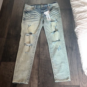 Ljusblå slitna jeans från Purple Brand - Säljer ett par ljusblå jeans från Purple Brand med tydliga slitningar och hål på framsidan. Jeansen har en straight passform och klassisk femficksdesign. Perfekta för en avslappnad och trendig look.