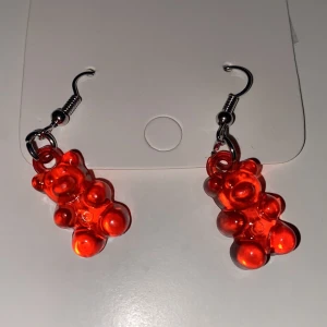 Röda örhängen med gummibjörn design INGA PLUPPAR - Unika röda örhängen godisliknande form. Hängande modell med metallkrok. Perfekta för att addera färg och lekfullhet till din stil.