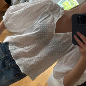 Vit blus med puffärmar från Kappahl - Säljer en söt vit blus från Kappahl med puffiga trekvartsärmar och diskret prickigt mönster. Blusen har v-ringning och små volangdetaljer vid halsen. Perfekt för en fräsch och somrig look!
