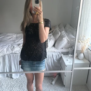 Svart spetsblus - Säljer en svart blus i spets med korta ärmar och rund halsringning. Blusen har ett transparent mönster och är perfekt att styla till både jeans och kjol. Superfin detalj med spetsen som ger en elegant känsla.