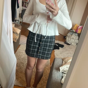 Svartvit rutig kjol med knappar - Säljer en svartvit rutig kjol med knappar framtill. Kjolen är kort och har en rak passform som sitter snyggt i midjan. Perfekt att styla med en enkel topp eller stickad tröja. Den är egentligen för liten för mig så den måste inte vara så högt upp.