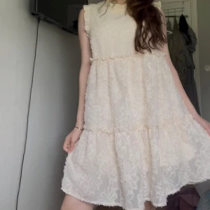  volangklänning - Säljer en söt vit klänning med volanger och spetsdetaljer. Klänningen är ärmlös och har en lös passform med flera lager och struktur i tyget. Perfekt för sommaren!💕 den är super bra skick och är midi lång jag är 167! 