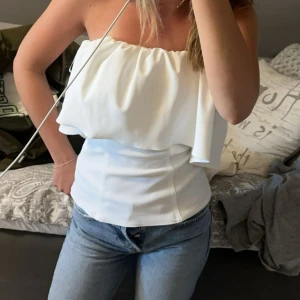 Vit axelbandslös croppad topp - Säljer en vit axelbandslös croppad topp med volang. Toppen har en luftig och somrig design, perfekt till jeans eller kjol. Säljer för att den inte kommit till användning. Endast använd en gång och köpte på Zara förra sommaren. Jag är 166 och den sitter bra på mig. Pris kan diskuteras 