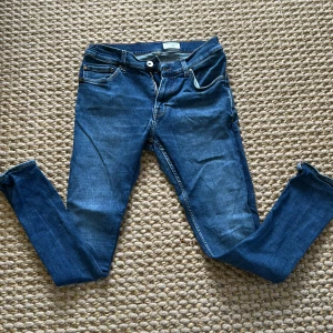 Blå jeans från Tiger of Sweden - Säljer ett par klassiska blå jeans från Tiger of Sweden, modell Evolve. Jeansen har normal passform, fem fickor och snygga kontrastsömmar. Perfekta för dig som gillar stilrena och tidlösa jeans med raka ben.