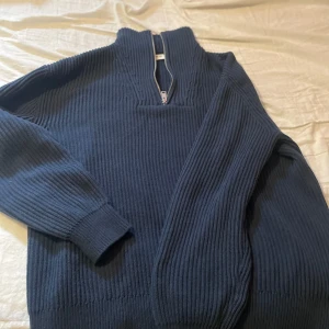 Mörkblå stickad tröja med dragkedja från Solid - Säljer en mörkblå stickad tröja från Solid i storlek L. Tröjan har hög krage med dragkedja och är ribbstickad för en snygg och bekväm passform. Perfekt för kyligare dagar och enkel att matcha med olika outfits.