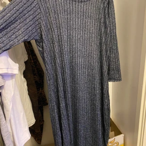 Glittrig ribbad långklänning - Säljer en snygg långklänning i glittrigt, ribbat material. Klänningen är svart med silvertrådar och har trekvartsärm. Perfekt för dig som vill sticka ut lite extra!