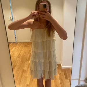 volangklänning med tunna axelband - Säljer en superfin ljusgul/cremevit klänning med flera lager volanger och tunna axelband i storlek S. Klänningen är kort och passar perfekt till sommaren. Klänningen är bara använd en gång så den är i mycket bra skick🩷